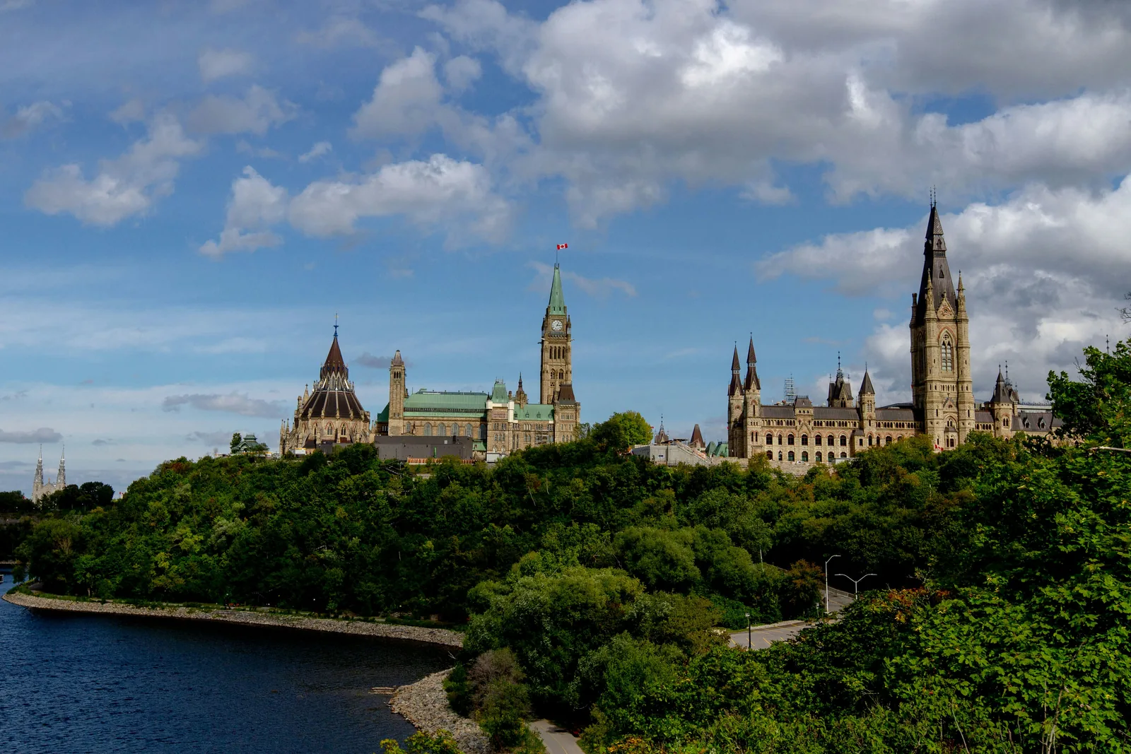 Parliament Hill above the Ottawa River, framed by green summer trees in Ottawa, Ontario